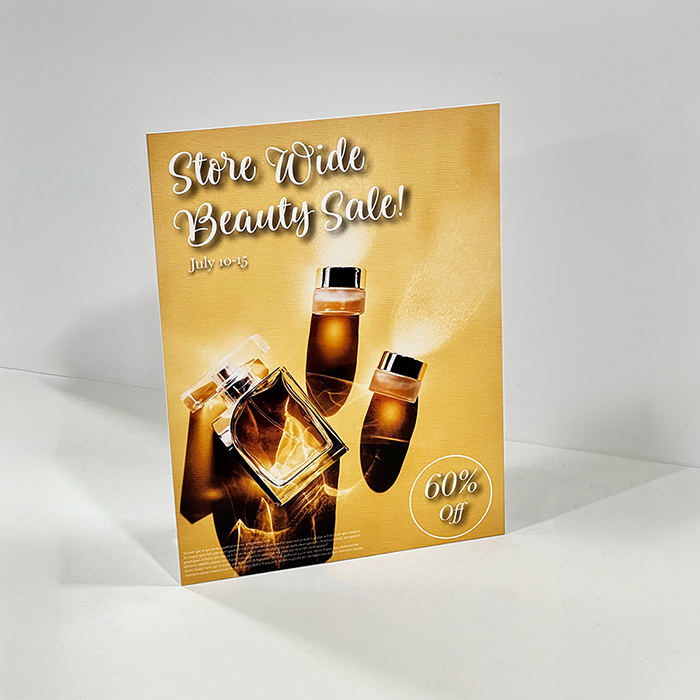 An easel back sign advertising a beauty sale with an image of perfumes on a gold background