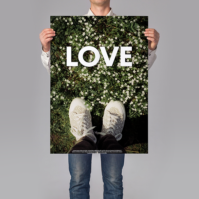 A person holding a poster with the word love in all capitals and a pair of shoes on grass